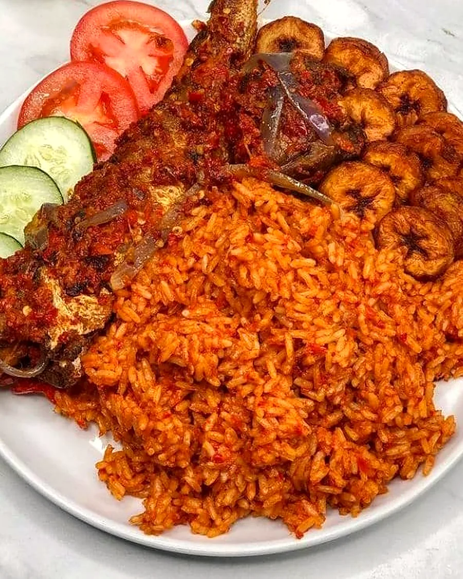 A plate of smoky jollof rice served with fried plantain, salad and grilled fish